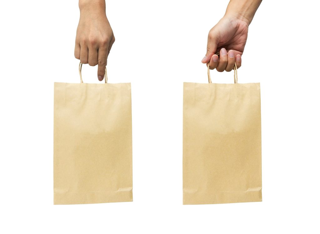 Hand holding brown paper bag on white background.